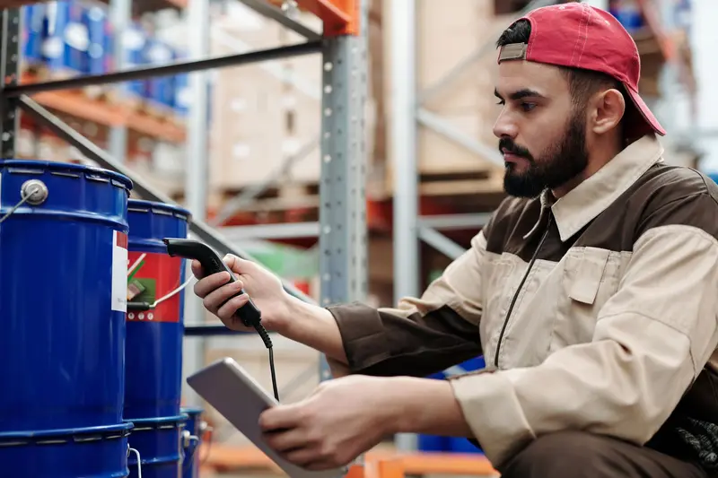 Warehouse worker using a handheld scanner next to shelves of blue drums