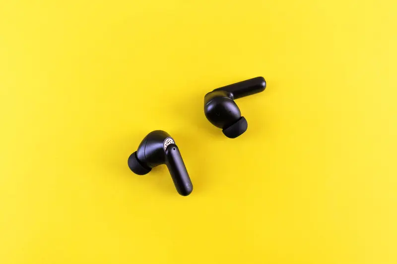 Two black wireless earbuds on a yellow background