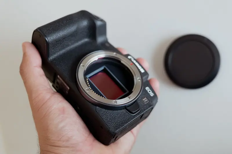 Hand holding a camera body without a lens, exposing the image sensor
