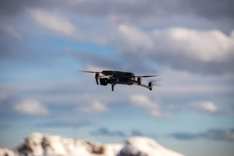 Four-propeller drone flying in front of clouds and mountains