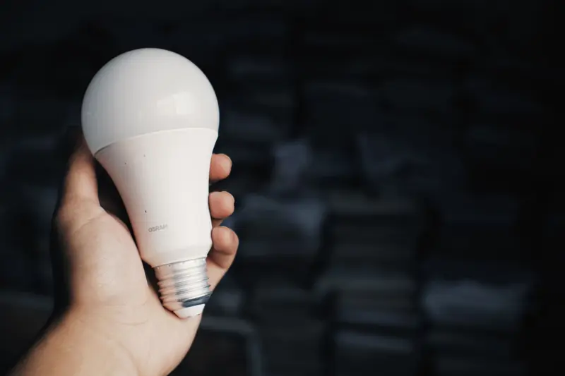 Hand holding a white LED bulb against a dark background