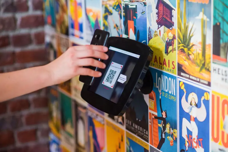 Hand holding a QR code up to a reader in front of a wall of colorful posters