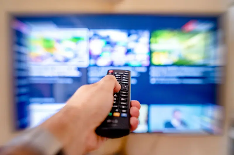 Hand pointing a remote control at a television showing a grid of programs