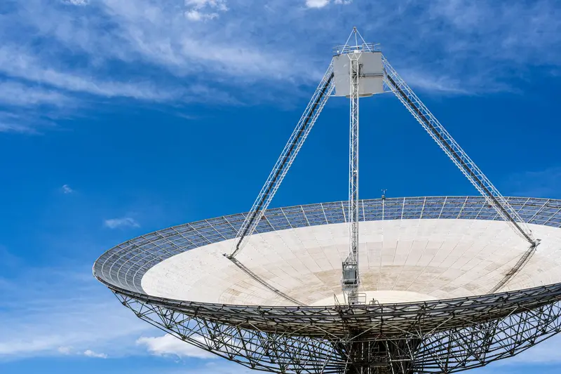 Large radio dish antenna held by a metal frame under a blue sky