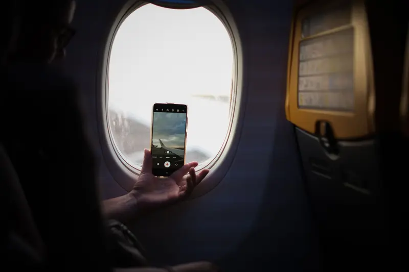 Passenger holding a smartphone up to the oval window of an airplane