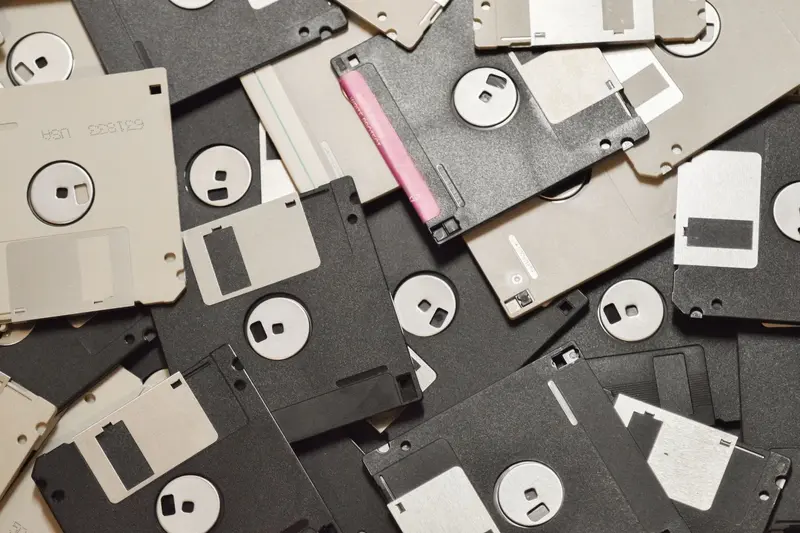 Pile of old floppy disks in different sizes and colors spread over a dark surface
